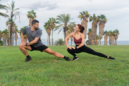 Sporty young adult couple stretching legs outside. Boyfriend and girlfriend doing a workout together...