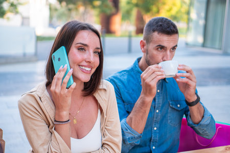 Two young adult couple, boyfriend and girlfriend, sitting in a terrace, the male is drinking a cofee...
