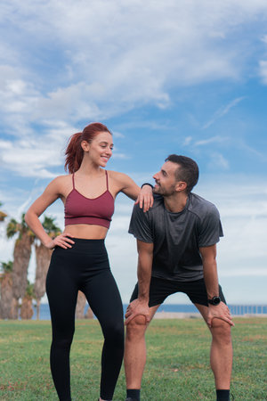 Vertical photo. Young sporty couple male and female resting exhausted with a hard training enjoying wellbeing and healthy lifestyle outdoors. Caucasian man and woman in sportswear relaxing and smiling after working outの写真素材