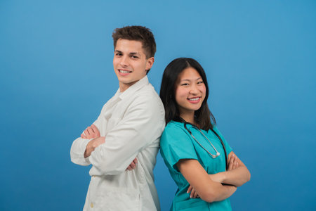 Confident healthcare professionals, male doctor and female nurse, standing back-to-back with arms crossed, smiling and demonstrating unity, trust, and expertise in a supportive medical environmentの写真素材
