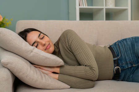 Young woman peacefully sleeping on a beige couch in a cozy living room, resting her head on a soft pillow, enjoying relaxation and tranquility during a quiet indoor moment.の写真素材
