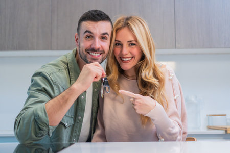 Excited young couple holding house keys, celebrating moving into their new apartment together,...