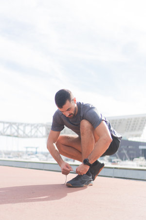 Determined Young Man Ties Shoelaces While Preparing for an Energetic Outdoor Workout Session to...