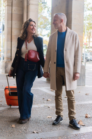 Happy couple walking hand in hand, enjoying their quality time together while traveling with stylish luggage and fashionable outfits that reflect their personalities and sense of adventureの写真素材