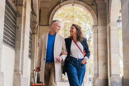 Happy couple enjoying a delightful stroll together while embracing a joyful moment filled with love and warmth, showcasing their stylish outfits and genuine connection as they walk side by side.の写真素材