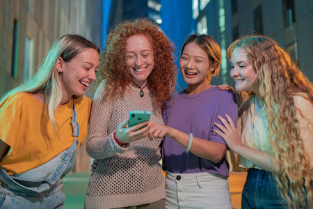 Four joyful friends sharing exciting moments while looking at a smartphone together, showcasing their vibrant personalities and joyful expressions in a lively social interactionの写真素材