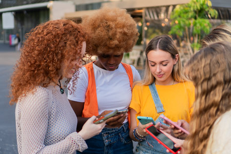 Diverse group of friends joyfully engaging with their smartphones while exploring interesting content together in a lively outdoor setting full of energy and excitementの写真素材