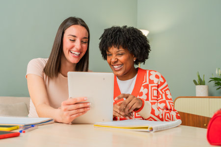 Two joyful women using a tablet to explore an exciting application together while sharing laughter and smiles in a delightful home setting filled with warmth and connectionの写真素材