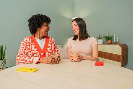 Two cheerful friends enjoying a delightful conversation while sipping warm beverages and sharing joyful moments at a cozy table, creating a warm and friendly atmosphere of connection and laughterの写真素材