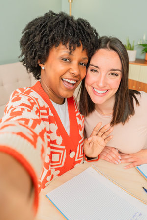 Two cheerful women enjoying a fun and lively moment together while taking a selfie with warm smiles and genuine laughter that captures the essence of friendship and joy in their engaging expressionsの写真素材