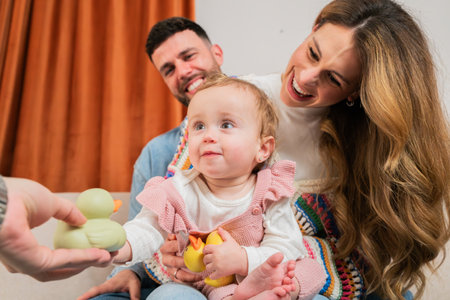 Joyful family moment as baby reaches for a colorful rubber duck toy during playful interaction with loving parents in a warm and inviting atmosphere of laughter and happinessの写真素材