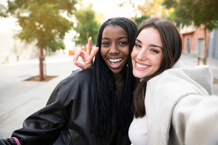 Two young multicultural friends taking selfie and having fun together - Caucasian and American Afro female frineds enjoying together.の写真素材