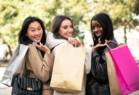 Three cheerful young women shopping in the city - Rear view of three happy beautiful young women with shopping bags in the city looking at camera - Fashion and friendship conceptの写真素材