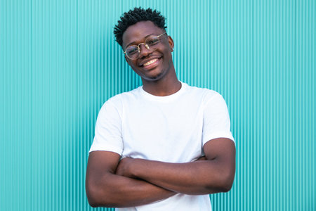 Happy young african american man smiling with arms crossed on turquoise background - Portrait of a...