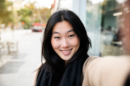 happy young smiling woman taking a self portrait photo in the city - portrait of young japanese woman taking a selfie outdoorの写真素材