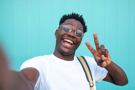 Selfie of cheerful handsome man in the street. Portarit of happy young man doing a selfie photo on the camera on a turquoise background wall.の写真素材