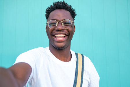Selfie of cheerful handsome man in the street. Portarit of happy young man doing a selfie photo on the camera on a turquoise background wall.の写真素材