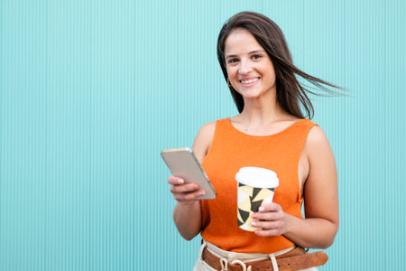 Beatiful woman smiling and looking at camera with a take away coffee and phone in turquoise wall - Portrait of happy young woman smiling and looking at cameraの写真素材