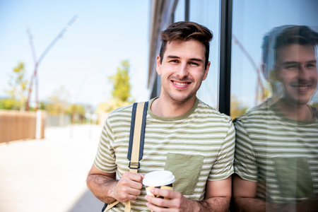 Happy young student smiling with backpack drinking a take away coffee at the campus.の写真素材
