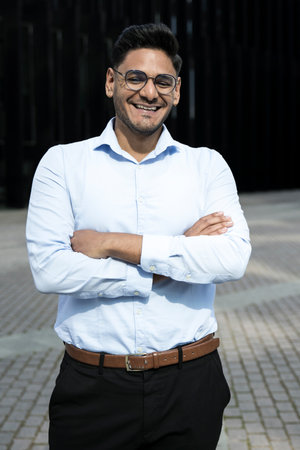 Smiling businessman arms crossed wearing glasses. Cheerful executive laughing in the street.の写真素材