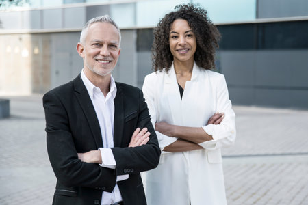 Senior businessman with businesswoman standing outdoors. Two executives with their arms crossed looking at the camera outside.の写真素材