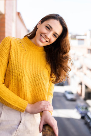 Close up of young smiling girl at leaning on a balcony on a sunny day. Cheerful woman staring at camera with a cute smile against an urban background.の写真素材