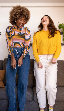 Multiracial young funny women dancing and laughing in their apartment. Happy and excited couple of girls celebrating in their living room.の写真素材