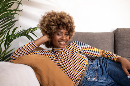 Happy young woman sitting on sofa at home and looking at camera. Portrait of beautiful woman in relaxing on armchair. Portrait of beautiful girl resting and relaxing on couch.の写真素材