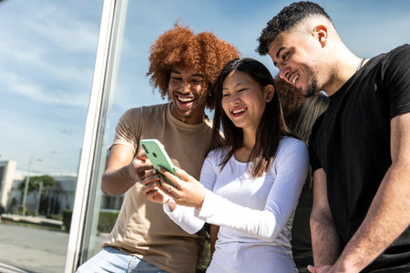 Three young diverse people looking at a smartphone standing int the street.Two young men smiling and watching at the phone of a happy woman.の写真素材