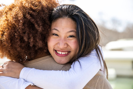 Close up of a young happy woman hugging a curly hair man. Lovely lady smiling while embracing a guy outdoors.の写真素材