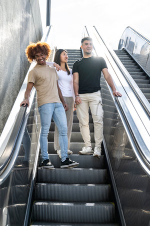 Multiracial group of friends laughing and going down an outdoor escalator. Three happy young people smiling and looking relaxed walking down of stairs in the street.の写真素材