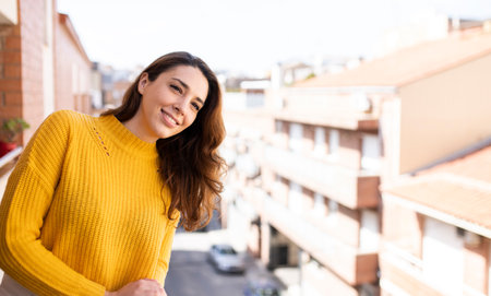 Portrait of young smiling woman looking away standing with a city background. Cheerful female looking satisfied on a balcony.の写真素材