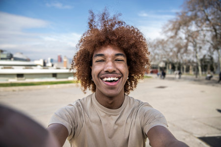 Happy handsome man smiling relaxed and looking at camera in the street taking a selfie. Relaxed happy man laughing and staring and holding the camera standing outdoors.の写真素材