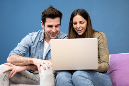 happy young couple sit on couch and using laptop. Cheerful couple smiling and searching on computerの写真素材
