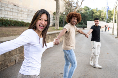 Three diverse and confident friends holding hands together. Multiracial group of people laughing and holding hands in a line. Focus on first woman.の写真素材