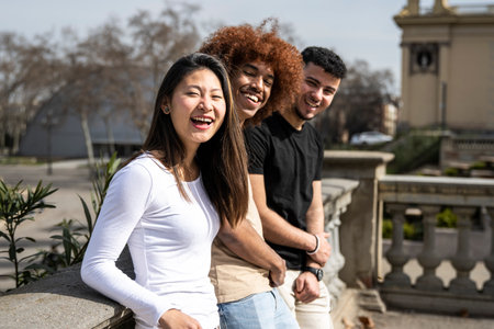 Multiracial group of young laughing people standing on a park looking at the camera. Three diverse happy friends having fun together outside staring at camera.の写真素材