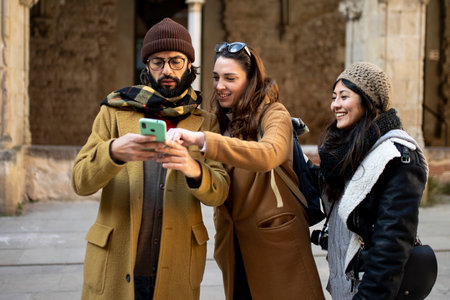 three happy friends using mobile phone on the street at winter. Group of students having fun outsideの写真素材