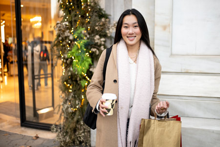 Young smiling woman standing in a shop with a cup of coffee during winter . Happy girl carrying shopping bags looking at camera.の写真素材