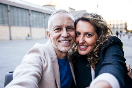 Affectionate mid adult happy couple having fun taking a selfie portrait together on the street. Middle aged man and woman friends smiling looking at camera.の写真素材