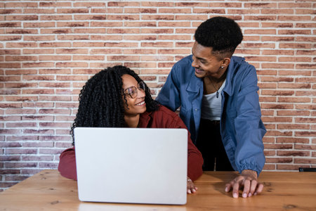Young couple using laptop in the living room. Satisfied man and woman smiling at each other while using a computer together at home.の写真素材