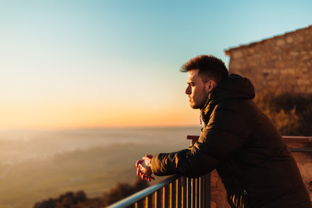 young adventurer resting on a railing on top of a hermitage, watching a beautiful cloudless sunset in the sky in Lleidaの写真素材