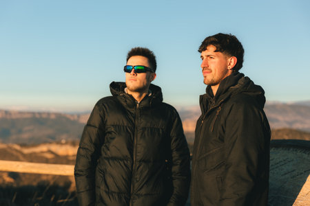 young adventurous couple with sunglasses watching a beautiful and warm sunset from a hermitage on...