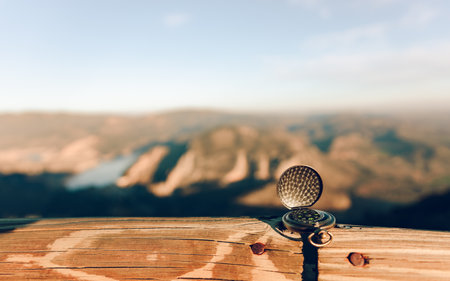 Golf ball on a wooden table with mountains in the background. Compass resting on the ground with the...