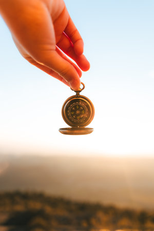 beautiful traveler's hand holding a compass backlit with a beautiful sunset in the background in...
