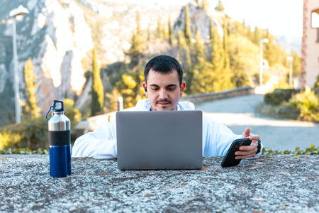 A young man with a laptop and a bottle of water in the mountainsの写真素材