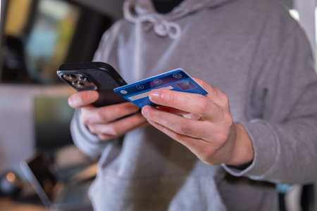Man in a gray suit standing and holding a credit card and using a laptop on the table to buy online or subscribe to some service. young businessman using internet while teleworking. e-bankingの写真素材