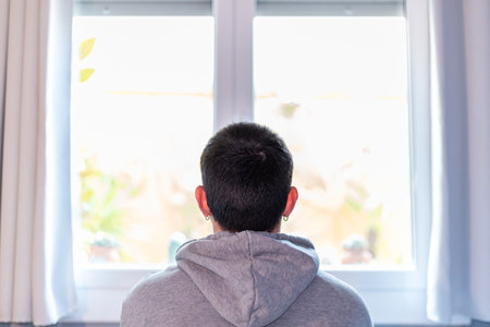 <p>Back view of a relaxed young man sitting alone on the sofa, looking out the window while thinking and enjoying life in solitude.</p>の写真素材