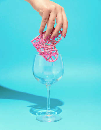 A woman's hand puts a heart in a wine glass, a combination of pink and blueの写真素材