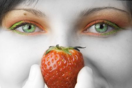 portrait of a young and cute brunette with big strawberry painted on her face and colored eyesの写真素材