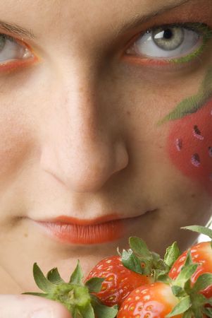 portrait of a young and cute brunette with big strawberry painted on her face and colored eyesの写真素材